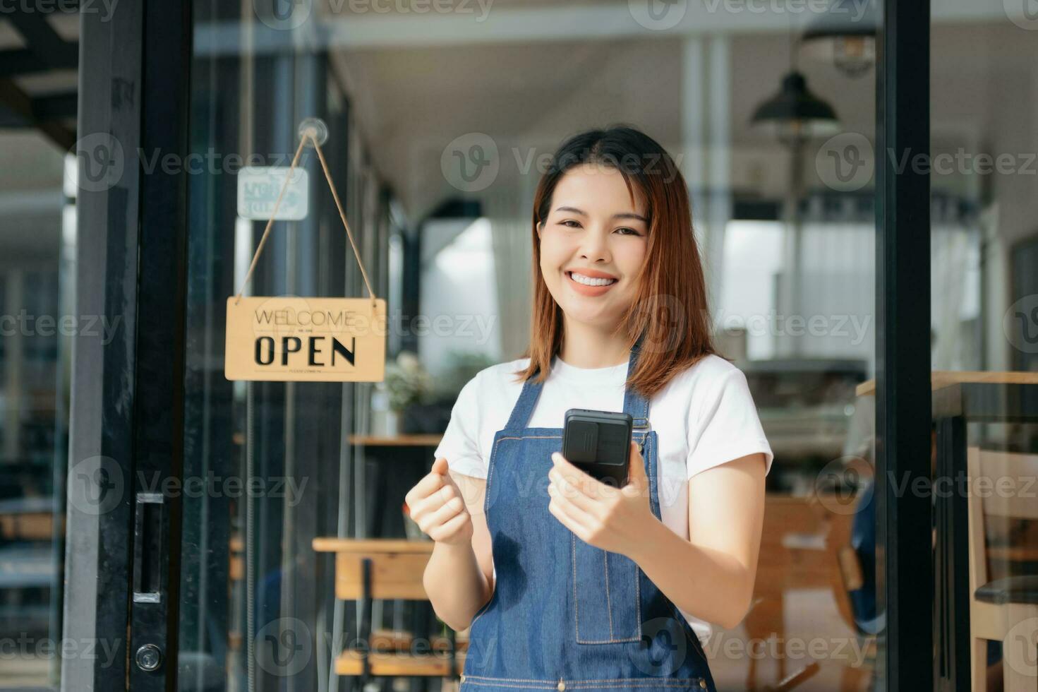 jung weiblich hängend ein herzlich willkommen Zeichen im Vorderseite von ein Kaffee Geschäft. schön Kellnerin oder Hostess halten ein Tablette vorbereiten im ein Restaurant. foto