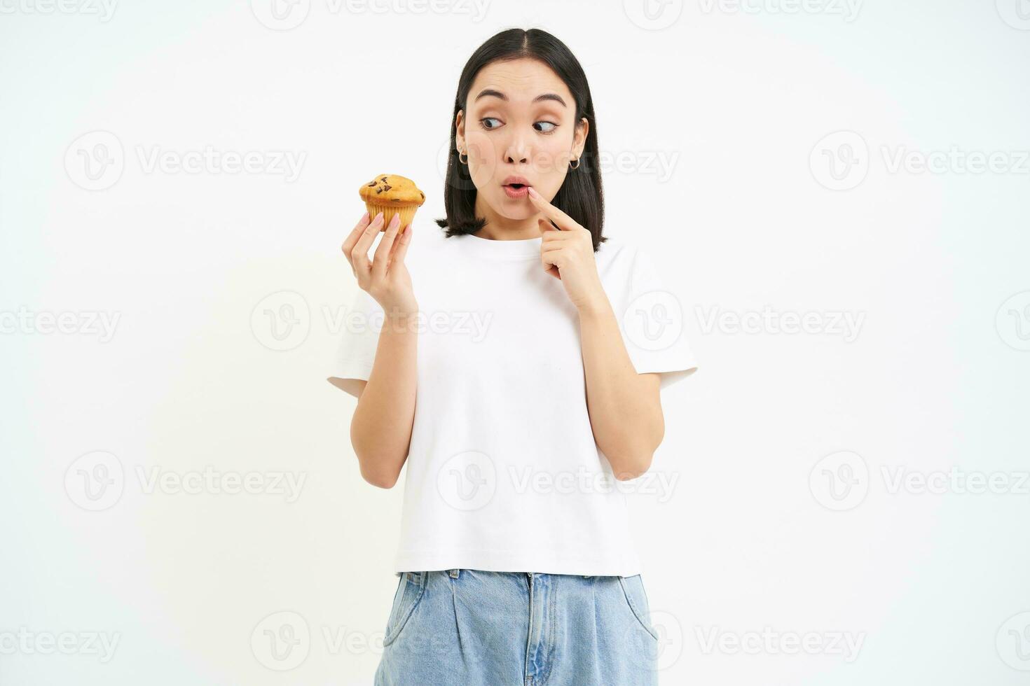 Bild von jung modern Frau mit Cupcake, sieht aus beim köstlich Gebäck von Bäckerei mit glücklich Gesicht, Weiß Hintergrund foto