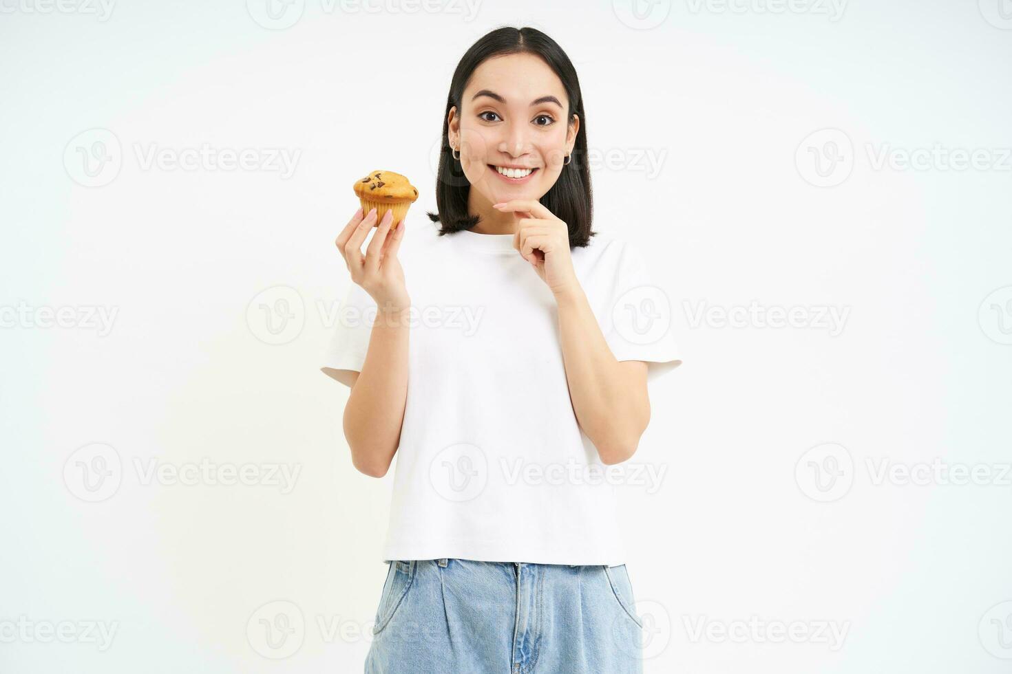 Bäckerei und Süßigkeiten. glücklich asiatisch Frau suchen beim lecker Cupcake, Essen Gebäck, Weiß Hintergrund foto