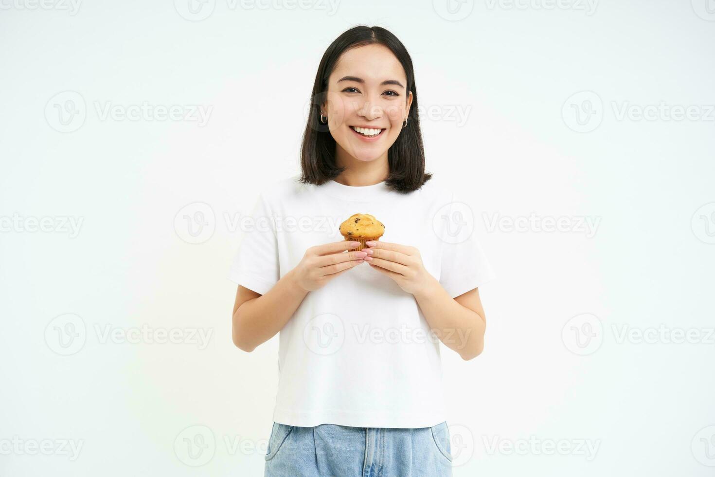 Porträt von Koreanisch Frau, zeigen Cupcake, Essen Kuchen und lächelnd, isoliert auf Weiß Hintergrund foto