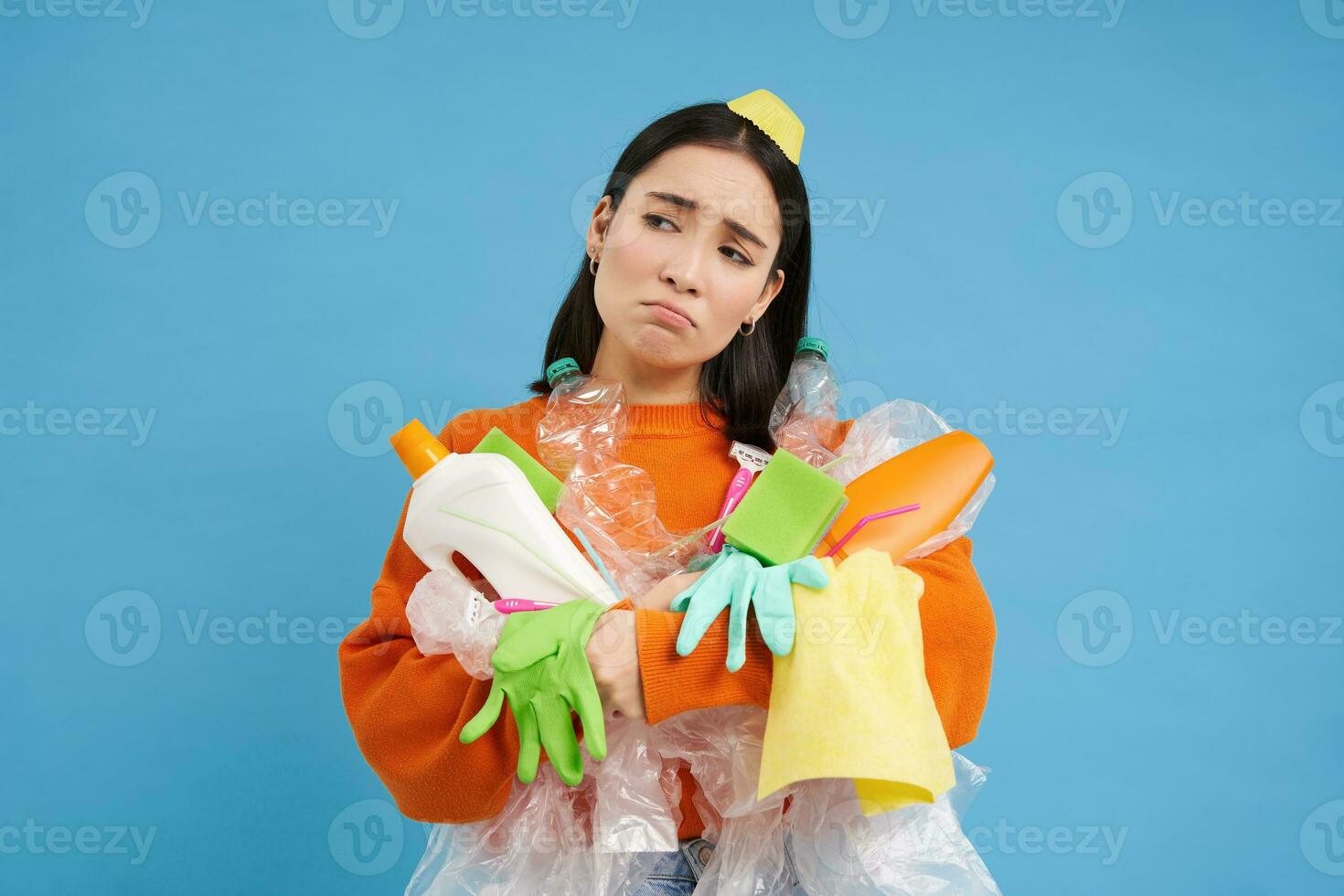 traurig asiatisch Frau halten Müll, leeren Plastik Flaschen und Abfall, müde von Recycling, Sortierung Müll, isoliert auf Blau Hintergrund foto