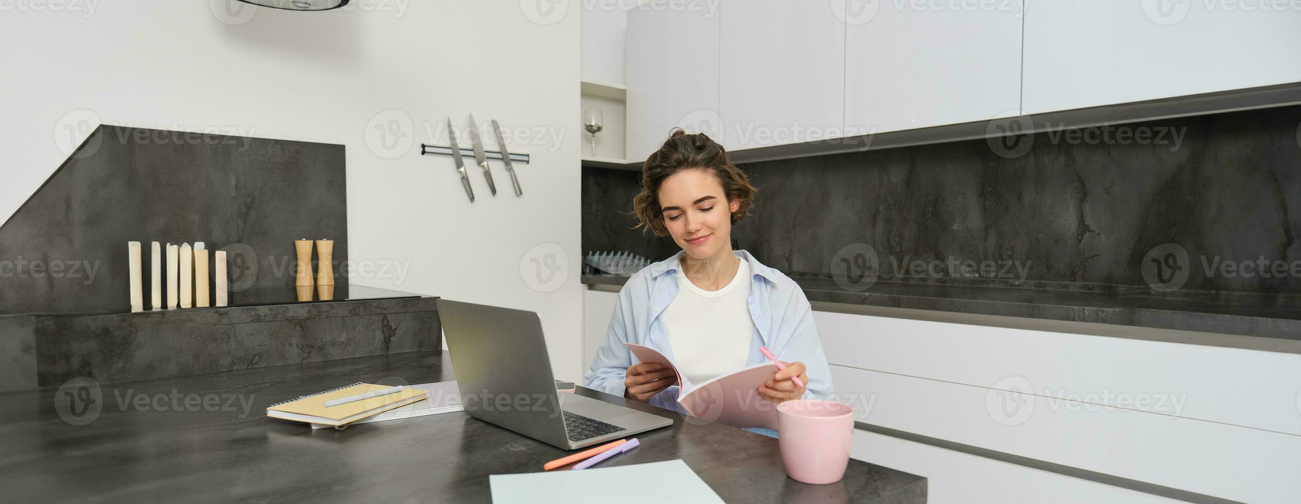 Porträt von jung schön Frau, Studien beim heim, flippt ihr Arbeitsmappe, funktioniert von heim, Verwendet Laptop zu lernen auf Fernbedienung, macht Anmerkungen während Webinar foto