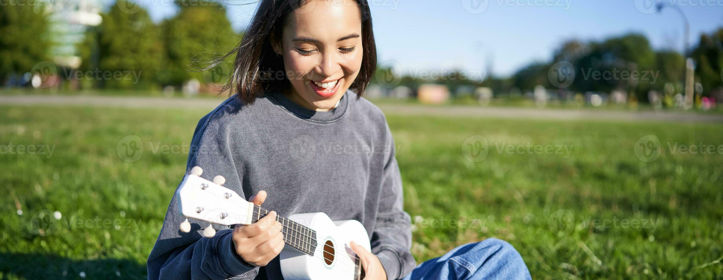 Porträt von asiatisch Mädchen Student, spielen Ukulele und Singen im Park, Sitzung allein auf Decke und genießen Herstellung Musik- foto