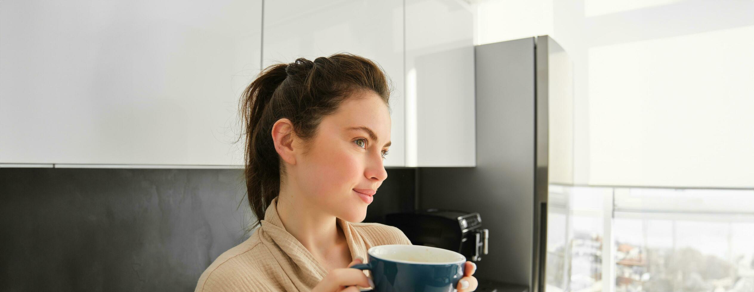 schließen oben Porträt von schön jung Frau, posieren im das Küche, suchen verträumt und nachdenklich, Nachdenken Morgen mit Becher von Kaffee, warten zum Frühstück foto