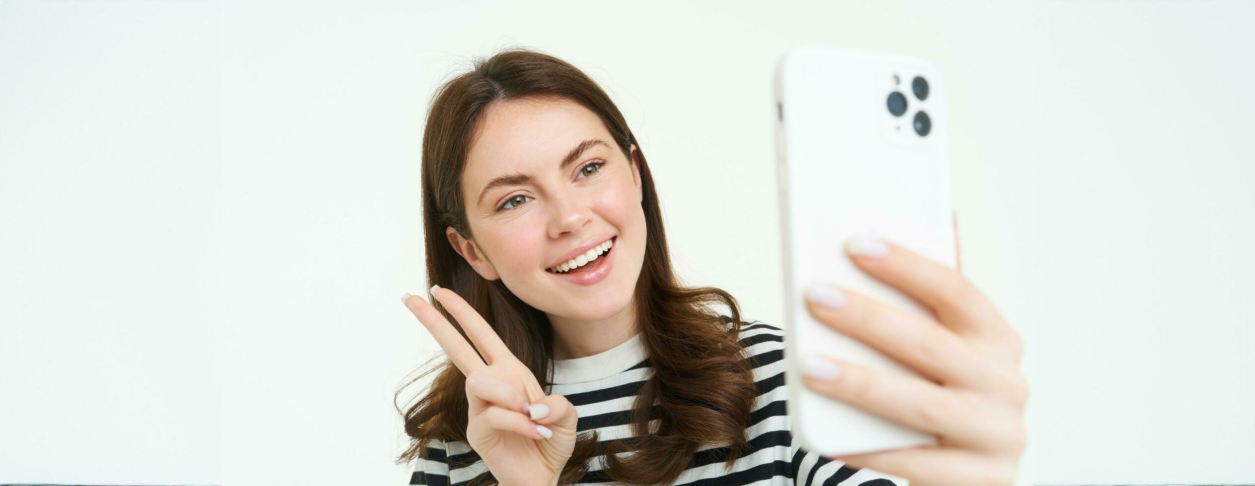 Porträt von jung Frau nehmen Selfies auf Smartphone, posieren zum Foto,. mit Handy, Mobiltelefon Telefon App zum nehmen komisch und süß Bilder, isoliert auf Weiß Hintergrund foto