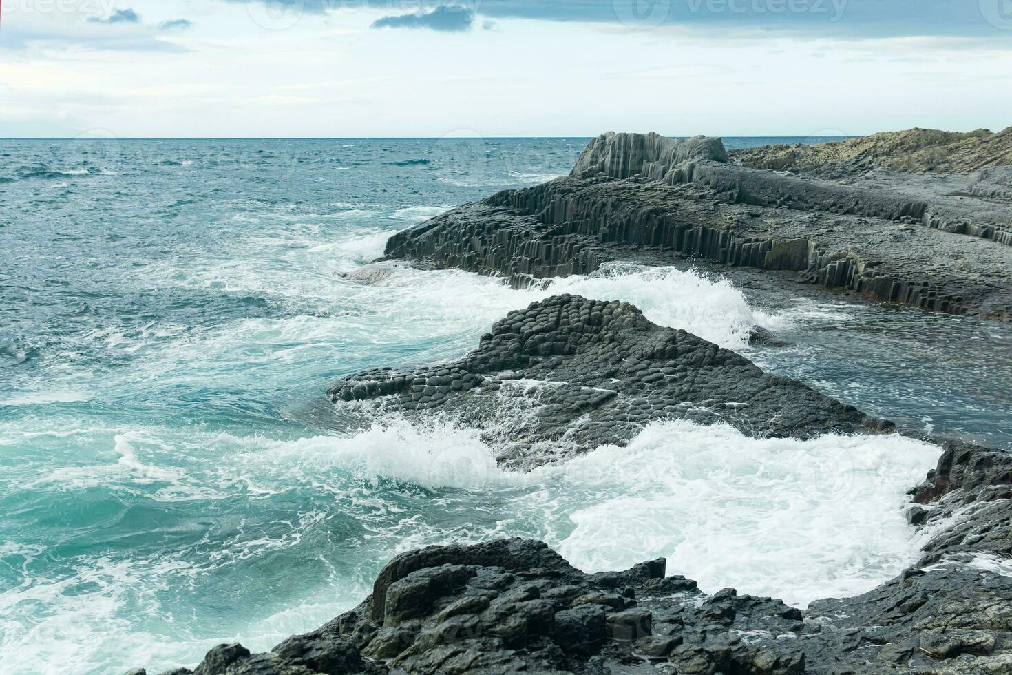 felsig Strand zusammengesetzt von säulenförmig Basalt gegen das stürmisch Meer, Küsten Landschaft von das Kuril Inseln foto