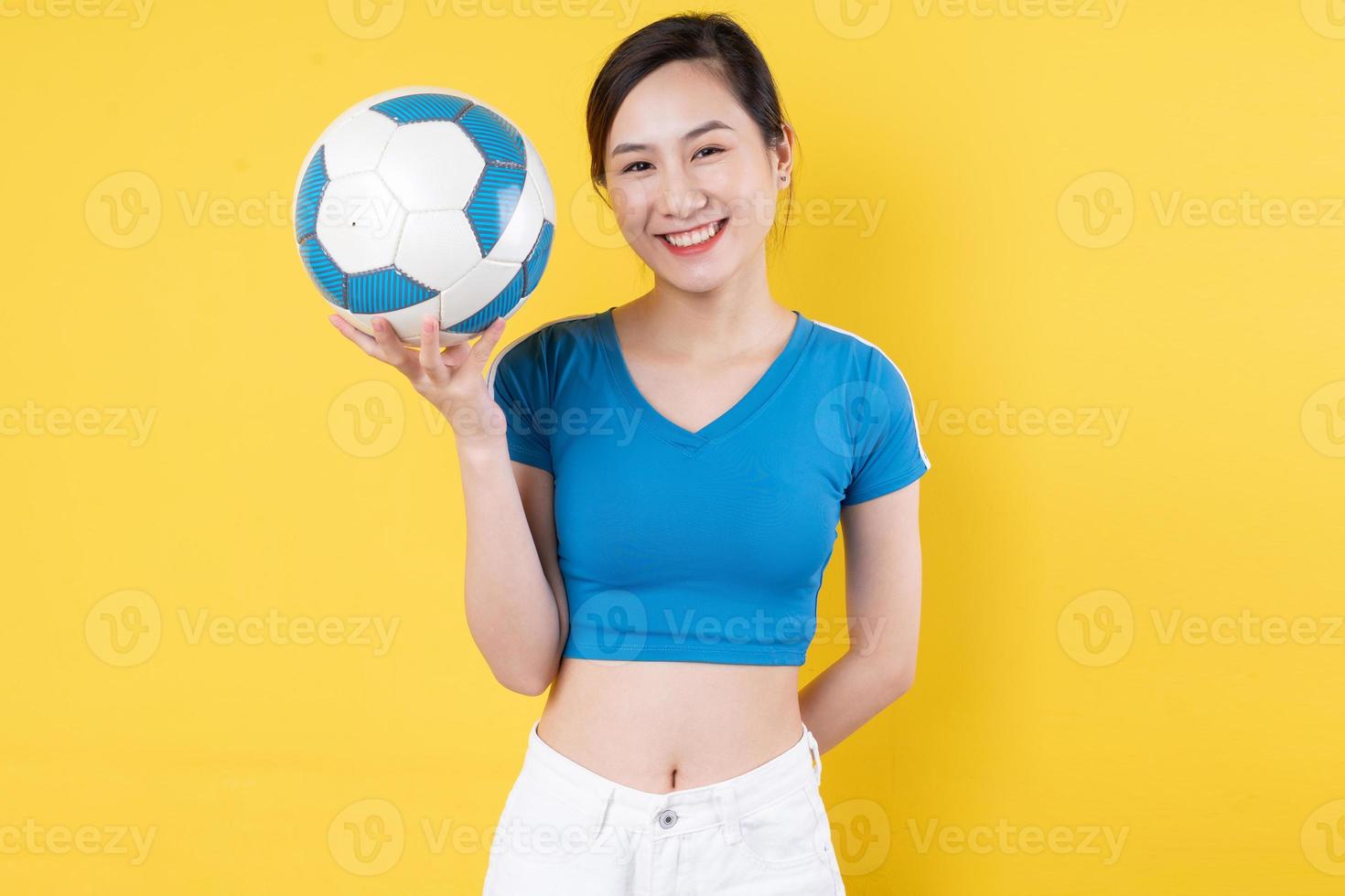 Porträt eines jungen dynamischen Mädchens, das Ball in der Hand hält, isoliert auf gelbem Hintergrund foto
