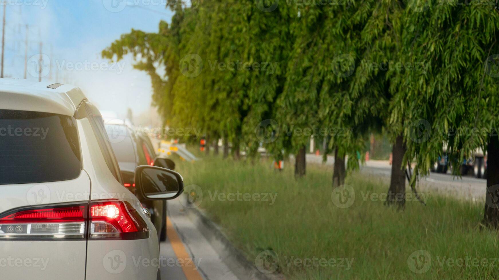 Rückseite Seite von Weiß Auto auf das Straße mit Wende auf Bremse Licht. Autos geparkt im ein Reihe, gestoppt beim ein der Verkehr Licht. auf das Seiten. Dort sind Gras Inseln mit hoch Bäume im das Mitte. foto