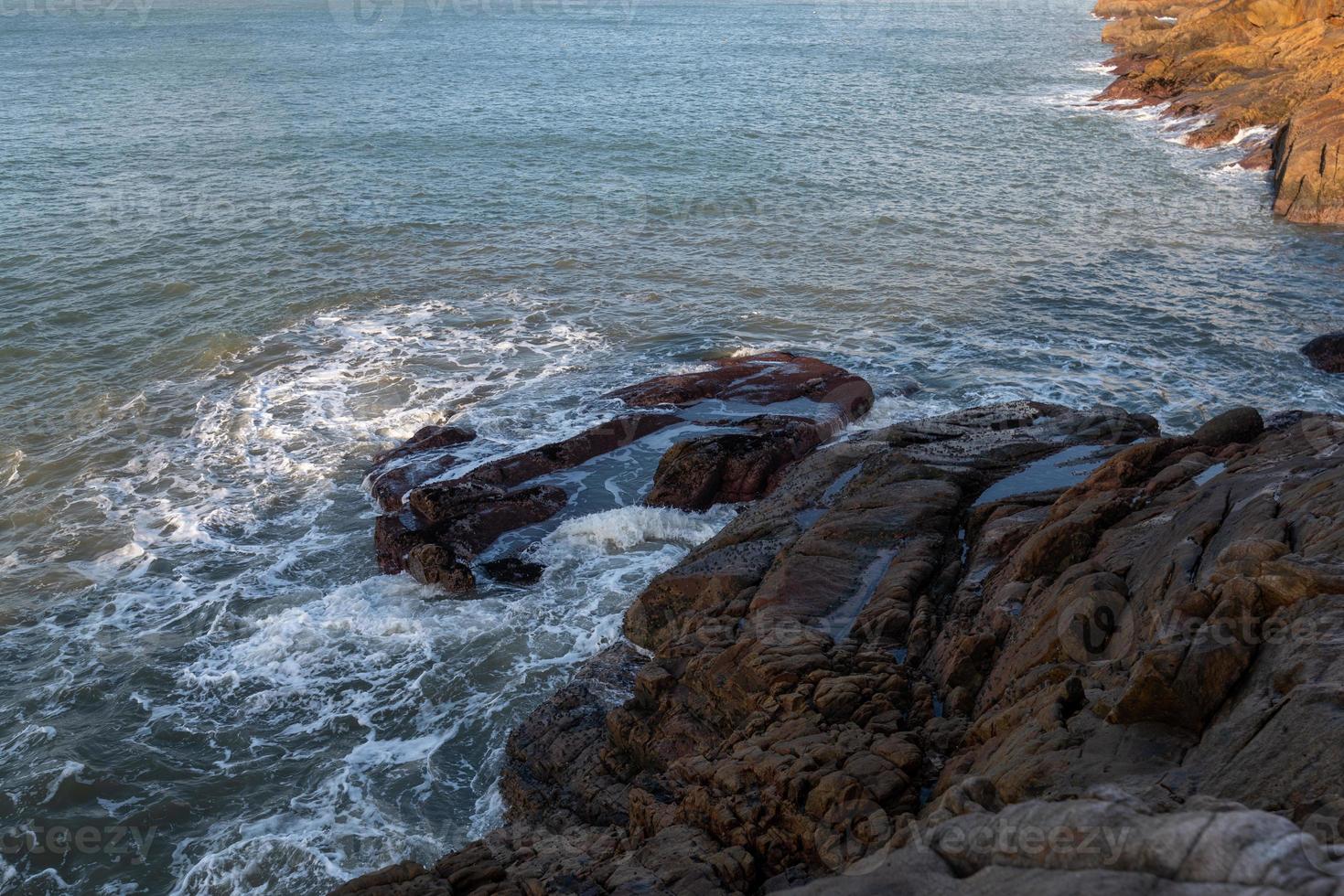 morgens scheint die sonne auf die felsen und wellen am strand foto