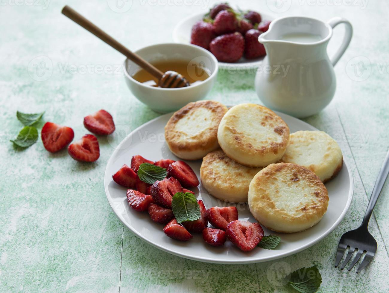 Quarkpfannkuchen, Ricotta-Krapfen auf Keramikplatte mit frischer Erdbeere. foto