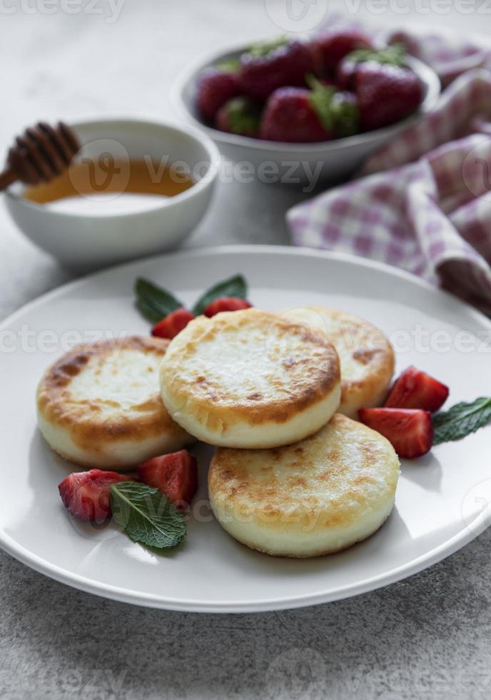 Quarkpfannkuchen, Ricotta-Krapfen auf Keramikplatte mit frischer Erdbeere. foto