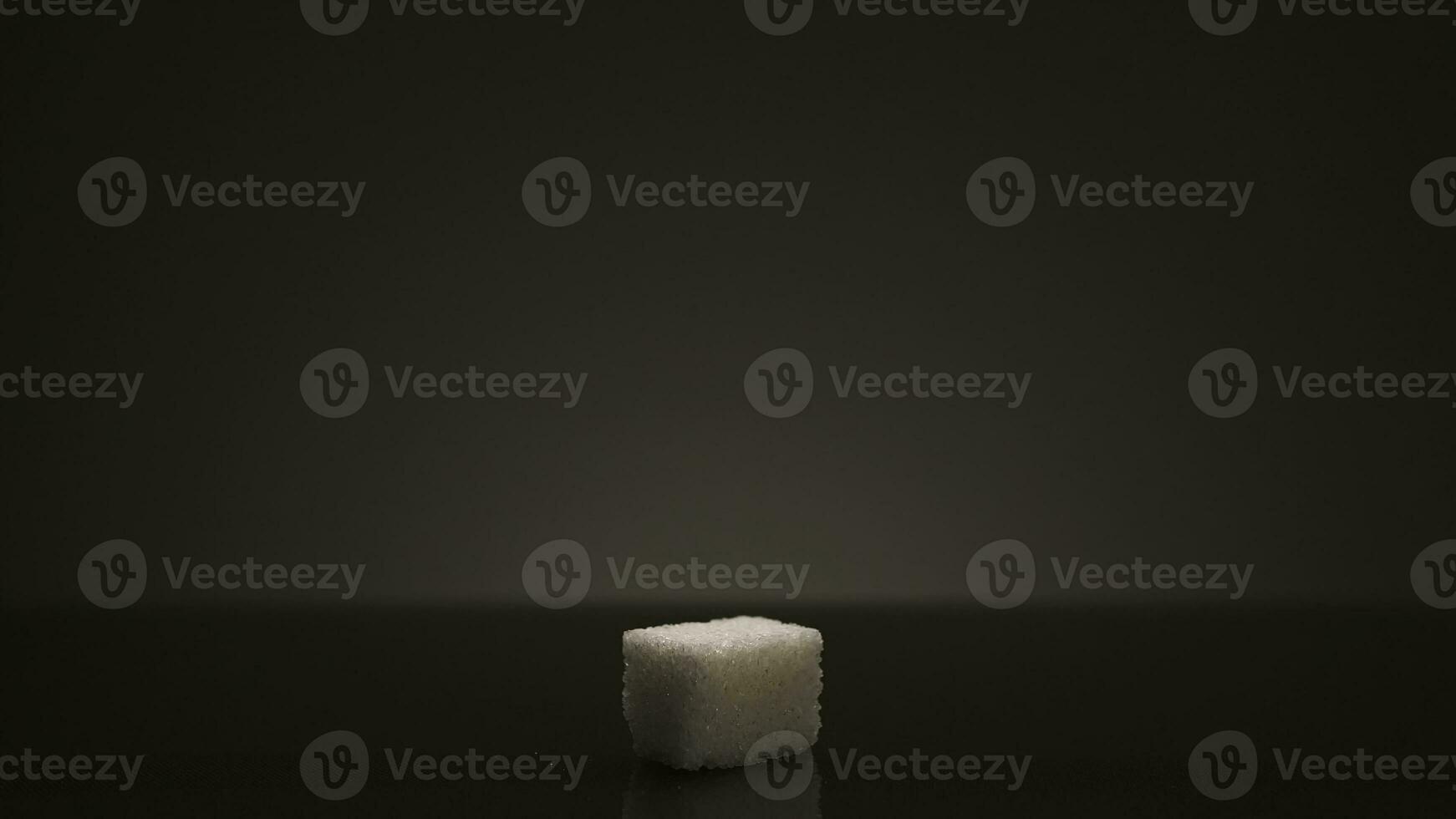 Single Würfel von Zucker isoliert auf dunkel grau Hintergrund. Lager Filmaufnahme. schließen oben von ein Weiß Zucker Würfel Stehen im das Schatten mit hell Licht leuchtenden Dann. foto