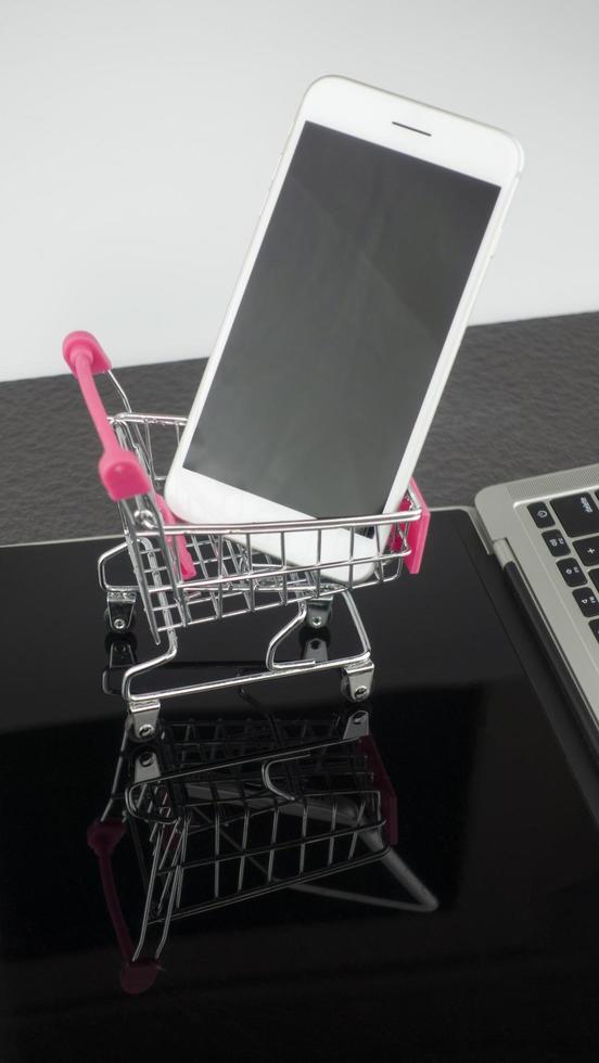 Smartphone auf dem Warenkorb mit Laptop auf dem Tisch, Online-Shopping-Konzept. foto