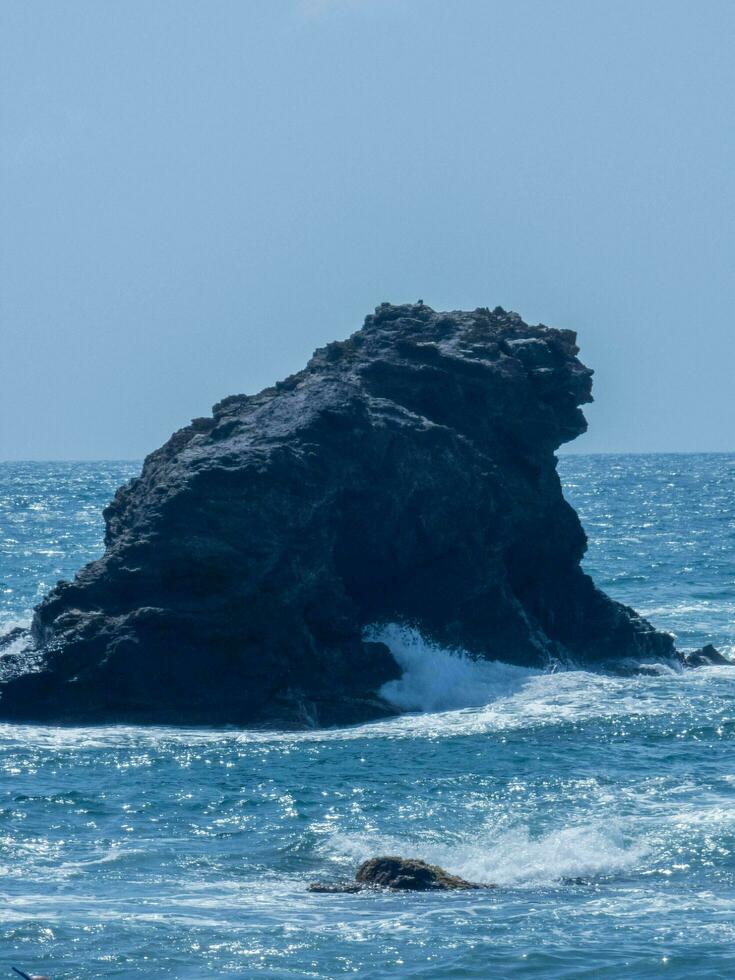 isoliert Felsen Formation im das Meer mit Wellen abstürzen um es unter ein klar Blau Himmel. foto