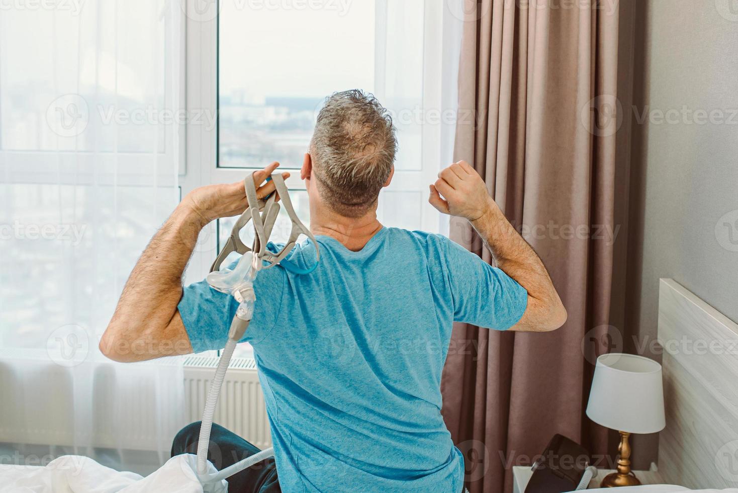 glücklicher ausgeruhter Mann mit chronischen Atemproblemen nach der Verwendung der CPAP-Maschine, die auf dem Bett im Schlafzimmer sitzt. Gesundheitsversorgung, CPAP, obstruktive Schlafapnoe-Therapie, Schnarchkonzept foto