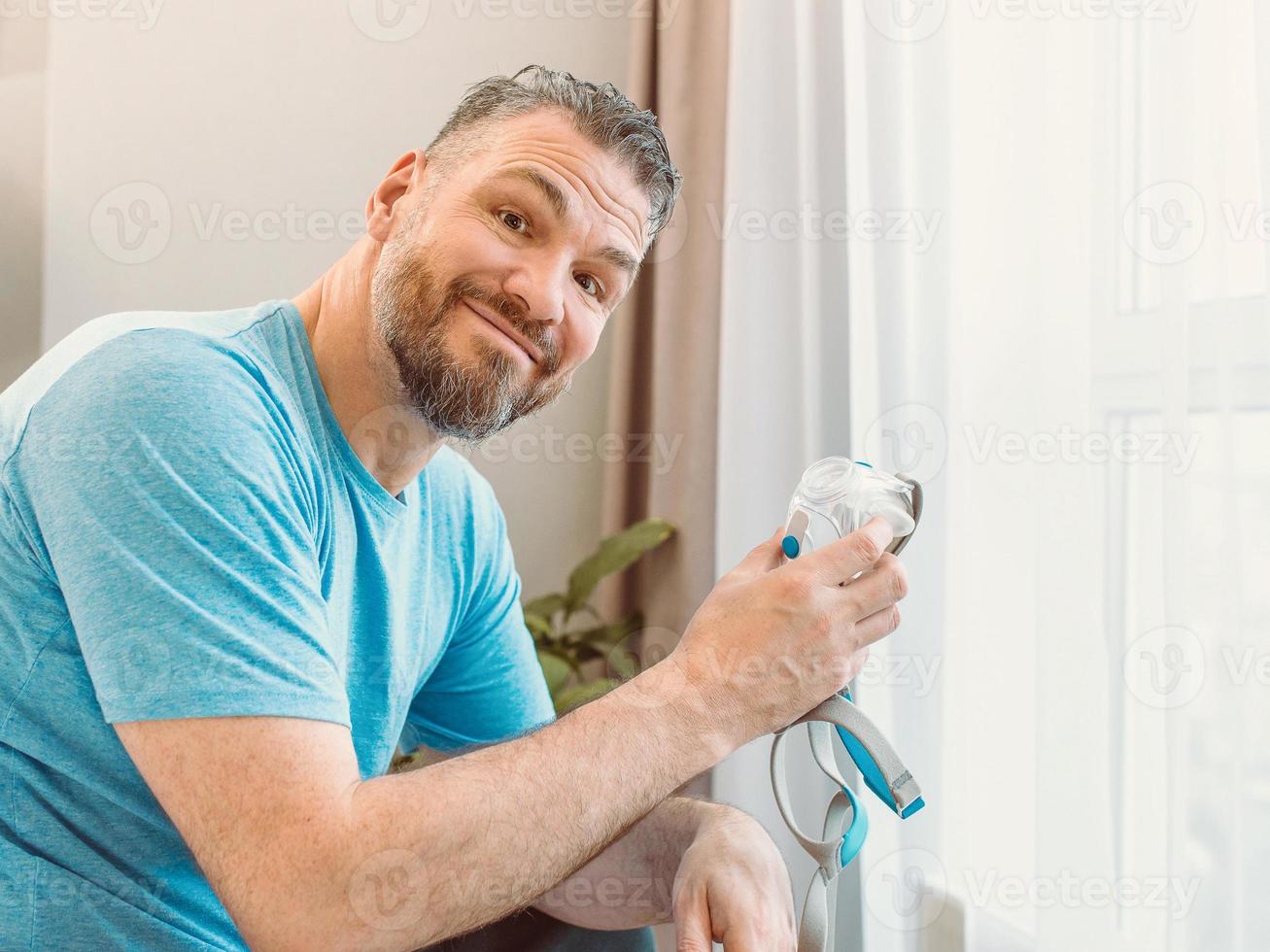 glücklicher ausgeruhter Mann mit chronischen Atemproblemen nach der Verwendung der CPAP-Maschine, die auf dem Bett im Schlafzimmer sitzt. Gesundheitsversorgung, CPAP, obstruktive Schlafapnoe-Therapie, Schnarchkonzept foto