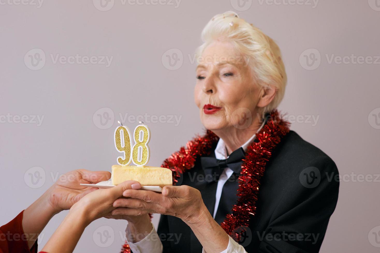 Fröhliche, stilvolle, achtundneunzig Jahre alte Frau im schwarzen Anzug, die ihren Geburtstag mit Kuchen feiert. Lifestyle, Positiv, Mode, Stilkonzept foto