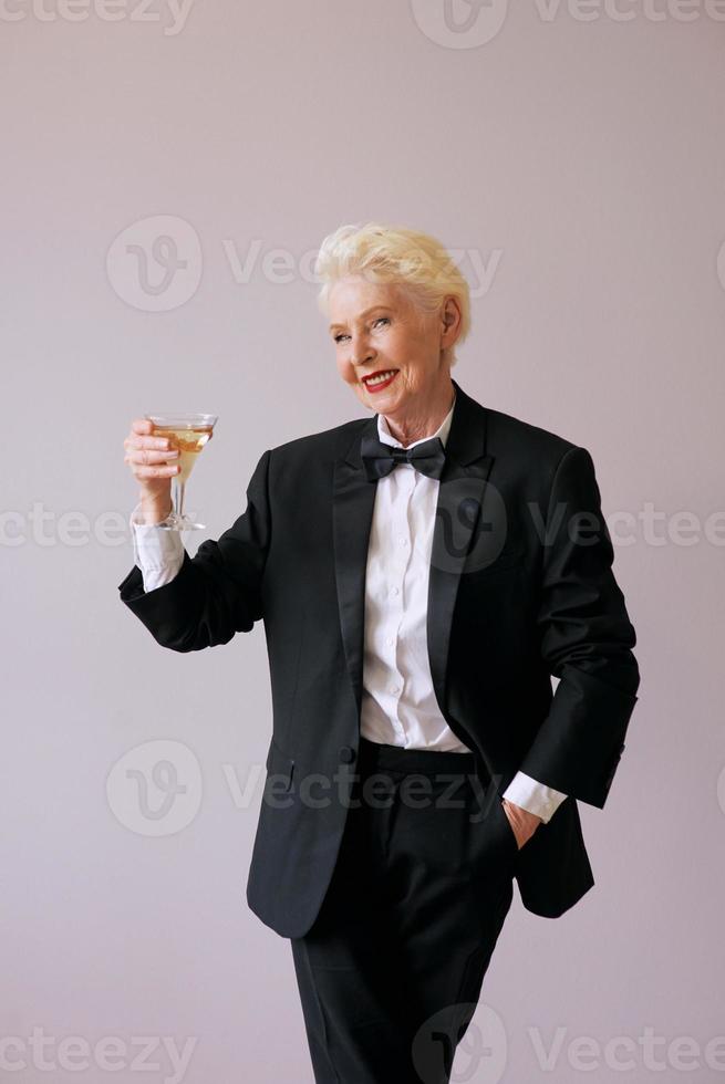 Stilvolle reife Sommelier-Senior-Frau im Smoking mit Glas Sekt. Spaß, Party, Stil, Lifestyle, Alkohol, Feierkonzept foto