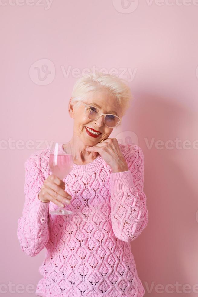 glückliche kaukasische ältere Frau in rosafarbenem Pullover aus Kaschmir, die Rose auf rosafarbenem Hintergrund trinkt. Feiern, Liebe, Ruhestand, ausgereiftes Konzept foto