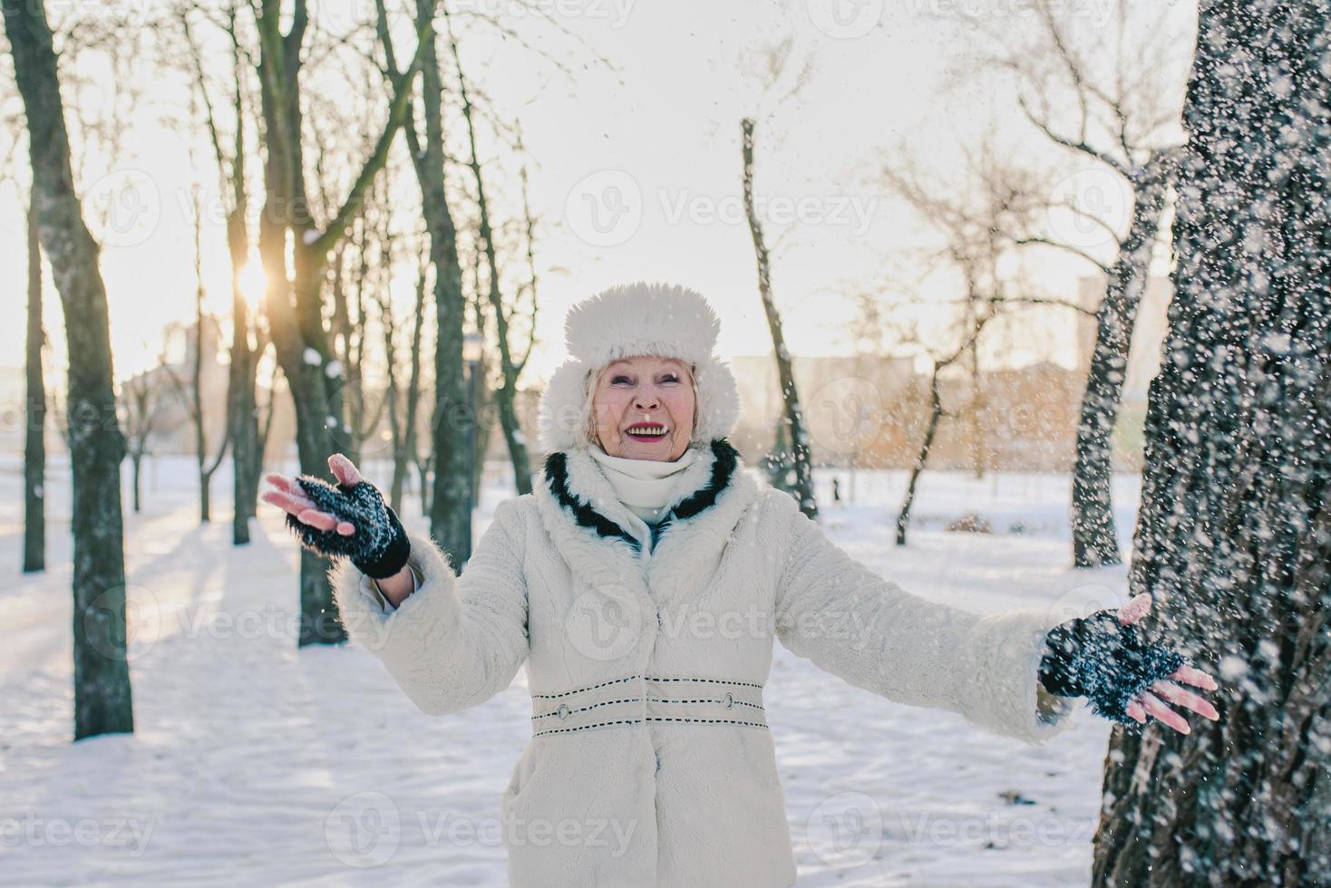 ältere Frau in weißem Hut und Mantel, die den Winter im Schneepark genießt. Winter, Alter, Saisonkonzept foto