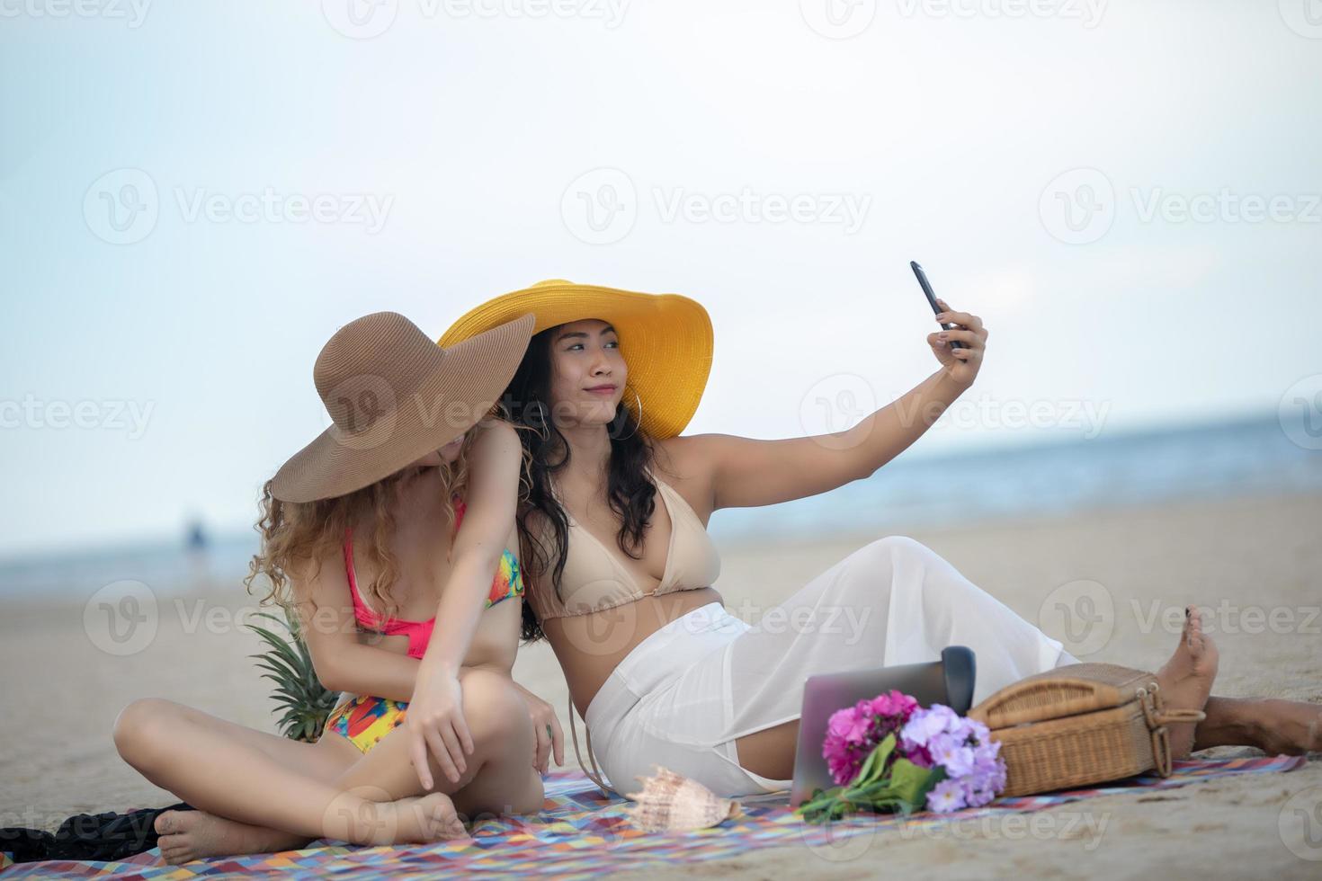 Frauen machen im Sommer Fotos und Selfies mit Freunden am Sandstrand.