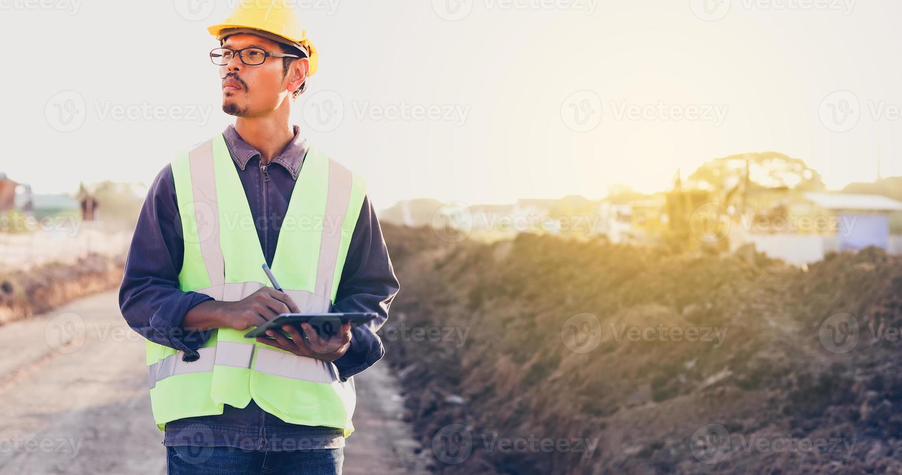 Asiatischer Ingenieur mit Bauarbeiterhelm mit Tablet-PC-Computer, der auf der Baustelle inspiziert und arbeitet foto