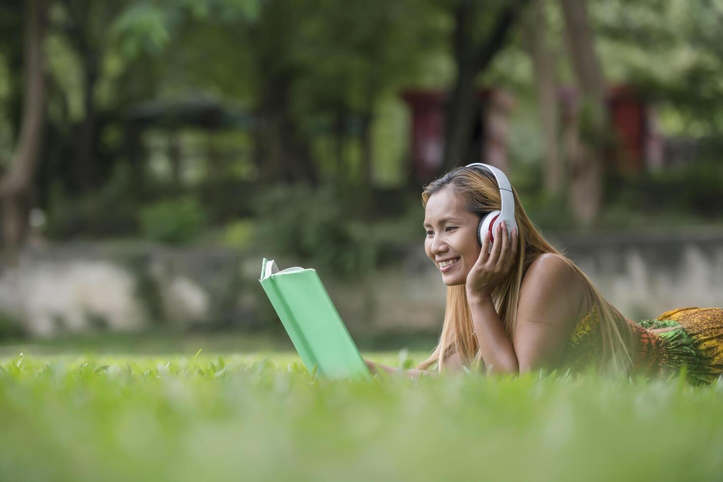 asiatische Frau hört Lieblingsmusik über Kopfhörer und liest ein Buch. glückliche Zeit und entspannen. foto