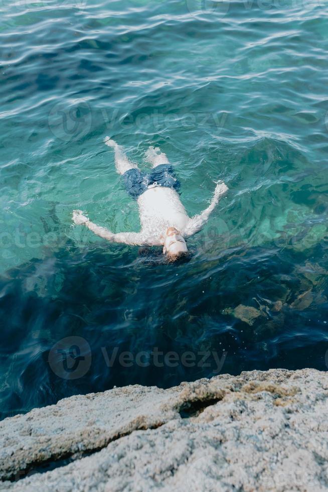 junger Mann, der während seines Urlaubs in Spanien im Meer schwimmt, kristallklares Meer, Kopierraum foto