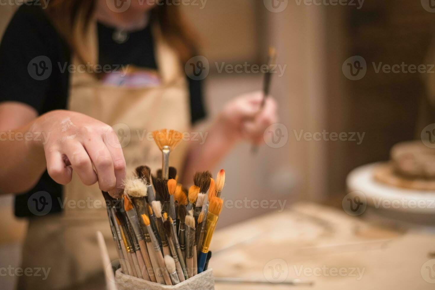 ein Mädchen im ein kreativ Werkstatt hält Bürsten zum Färbung ein Lehm Produkt foto