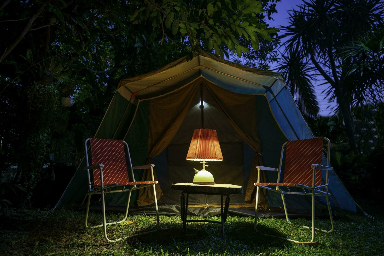 Jahrgang Kabine Zelt, Antiquität Öl Lampe auf ein hölzern Tabelle mit retro Stühle. beim Nacht im das Wald foto