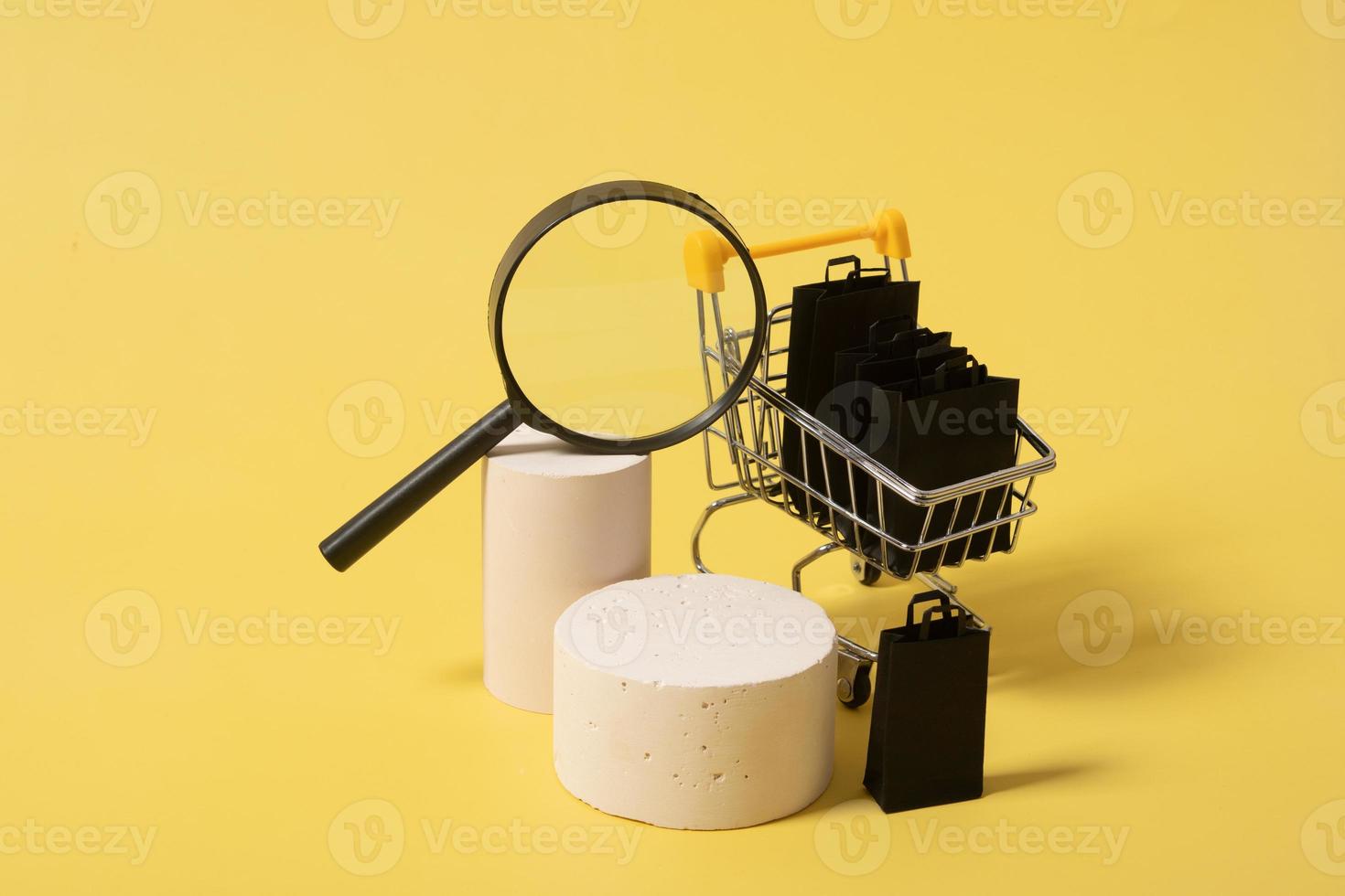 Leere Mock-Podien oder Podeste und Miniatur-Supermarktwagen mit Einkaufstüten im schwarzen Freitagsverkauf auf gelbem Hintergrund foto