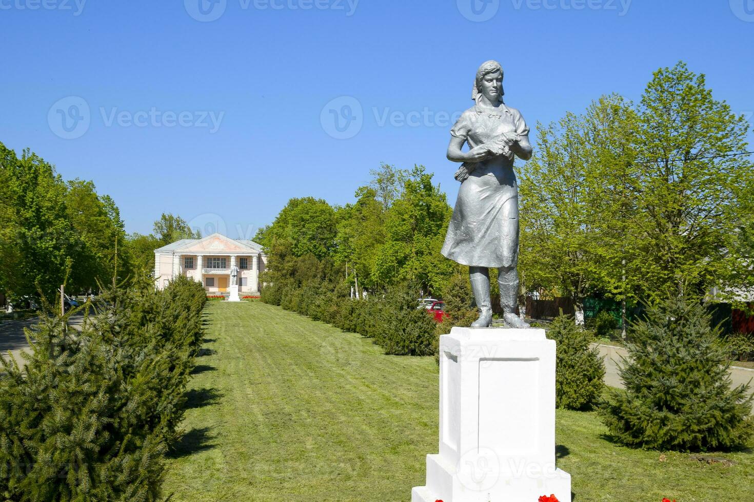 Statue von ein kollektiv Farmer auf ein Sockel. das Erbe von das Sowjet Epoche. ein Blume Bett mit Tulpen und jung Bäume im das Dorf von oktjabrski. krasnodar krai, krasnoarmeisky Bezirk. foto