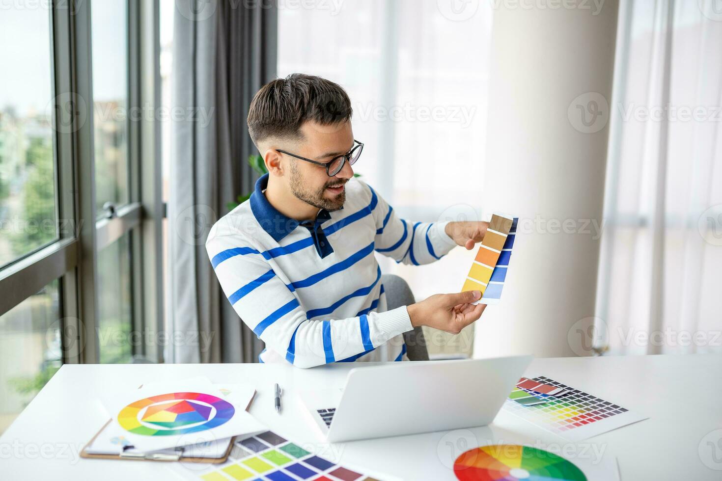 Netz Designer Arbeiten von heim, Sitzung beim Tabelle mit modern Laptop, suchen beim Farbe Proben, glücklich Mann Freiberufler genießen seine Fernbedienung Arbeit, Kopieren Raum foto