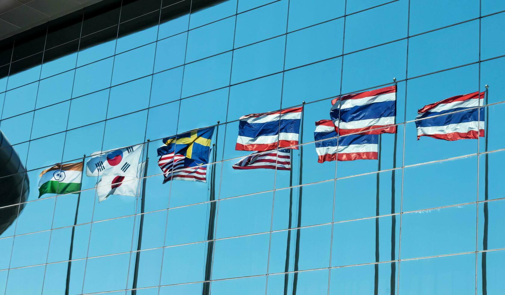 Indien Süd Korea Japan Malaysia Schweden Amerika und Thailand Flagge Pole Betrachtung auf Spiegel von Gebäude foto