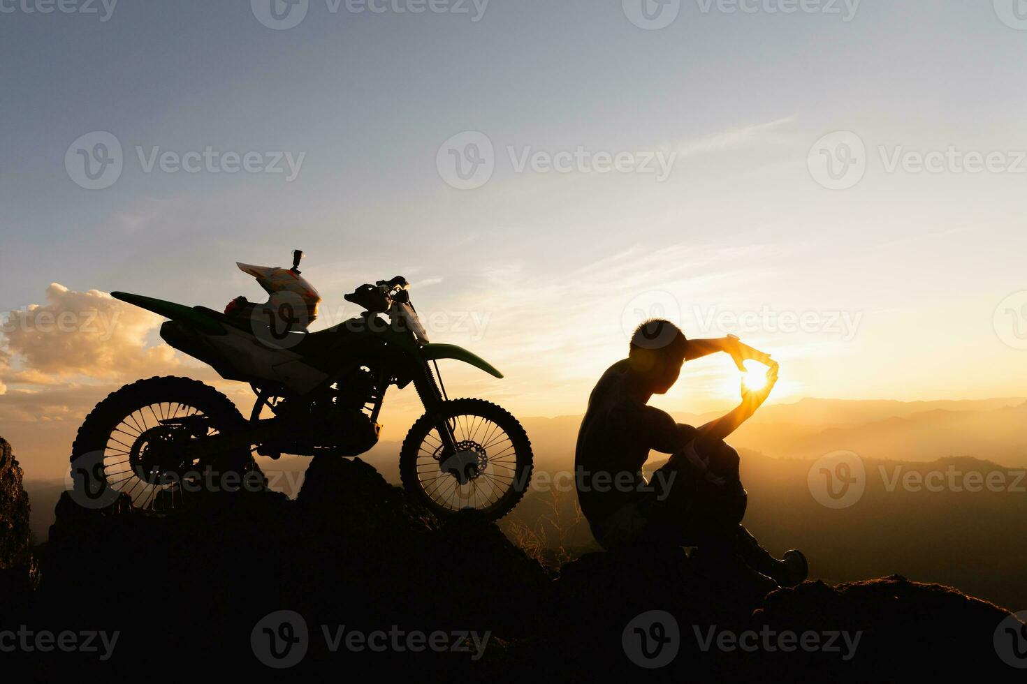 Mann mit Moto-Cross Fahrrad gegen schön Beleuchtung, Silhouette von ein Mann mit Moto-Cross Motorrad auf oben von Felsen hoch Berg beim schön Sonnenuntergang, Enduro Motorrad Reise Konzept. foto