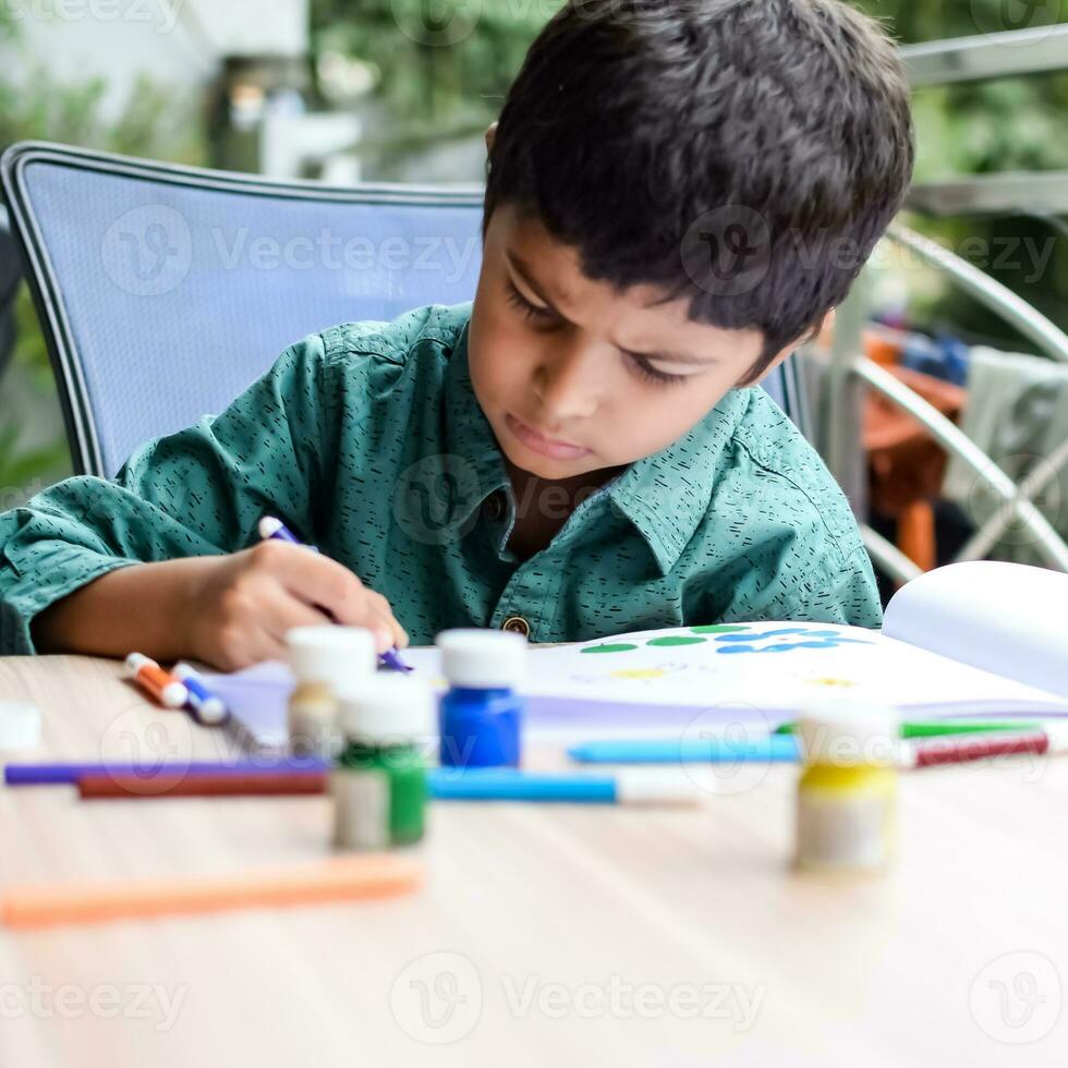 Clever indisch wenig Junge ausführen Daumen Gemälde mit anders bunt Wasser Farbe Kit während das Sommer- Urlaube, süß indisch Kind tun bunt Daumen Gemälde Zeichnung auf hölzern Tabelle foto