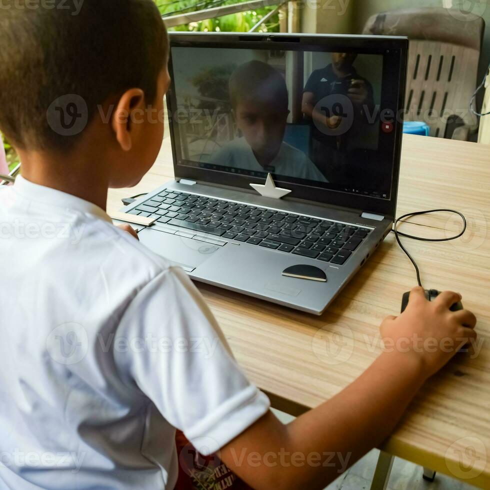 wenig Junge Sitzung beim Tabelle mit Laptop zum online Klasse im Klasse 1, Kind studieren auf Laptop von Zuhause zum Entfernung Lernen online Ausbildung, Schule Junge Kinder Lebensstil Konzept foto