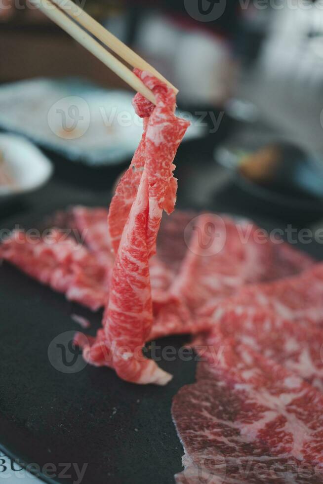 roh Rindfleisch mit hoch Marmorierung Textur wählen oben durch Holz Essstäbchen mit Hand zum Sukiyaki und Shabu. foto