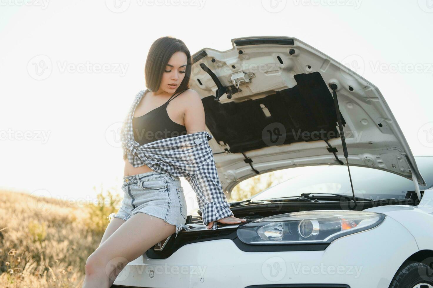das jung Mädchen Pleite das Auto und sie geöffnet das Kapuze und versucht zu Reparatur das Auto auf das Straße. ein Frau Anrufe auf ein Smartphone mit ein Auto Evakuierung Bedienung foto