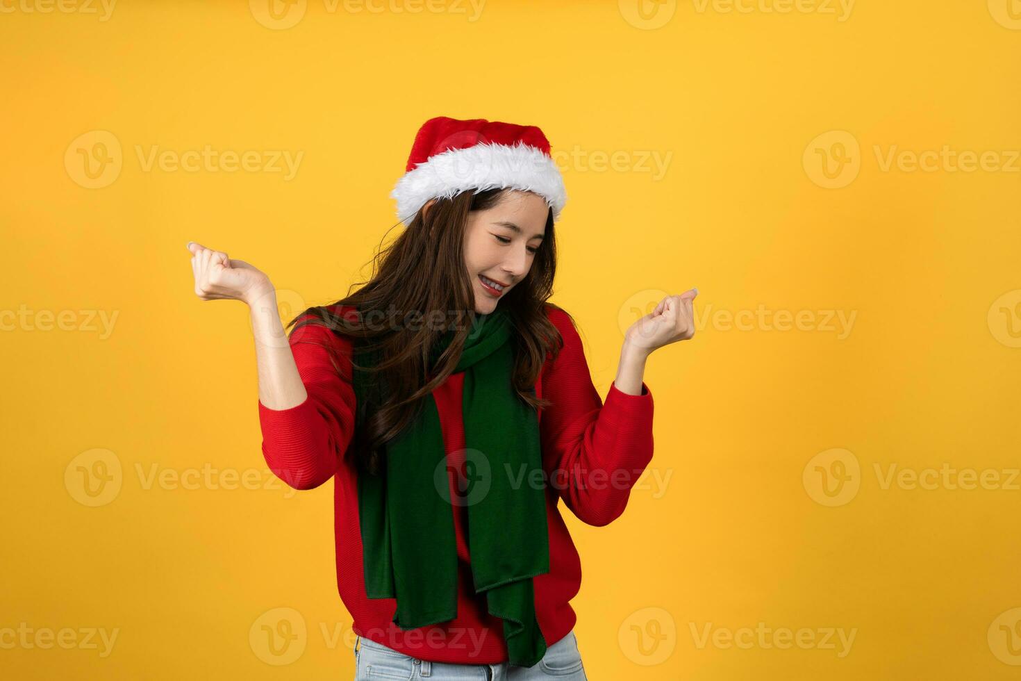 schön glücklich asiatisch Frau im rot Weihnachten Sweatshirt und Hut. sie ist aufgeregt und verkrampft beide Fäuste auf ein Gelb Studio Hintergrund. foto