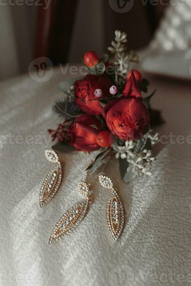 Einzelheiten von das Braut auf ein Sanft Rosa Stuhl, das Hochzeit Boutonniere und das Braut Schuhe sind Weiß. elegant Gold Ohrringe foto