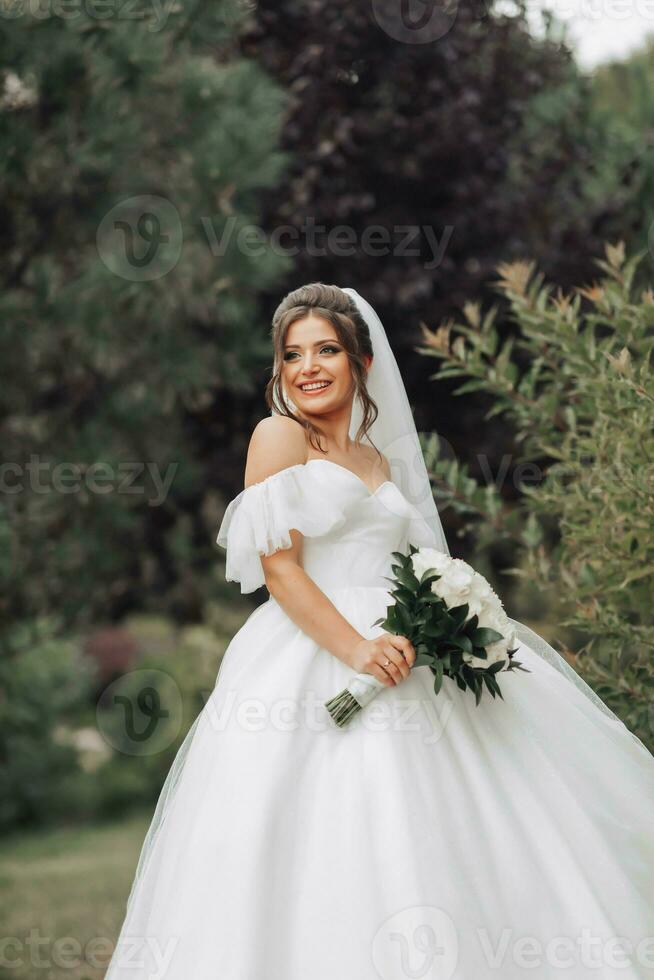 Hochzeit Foto. das Braut im ein voluminös Weiß Kleid und ein lange Schleier, lächelnd, wirbelnd mit ein Strauß von Weiß Rosen, halten ihr Kleid. Porträt von das Braut. schön bilden und Haar. foto