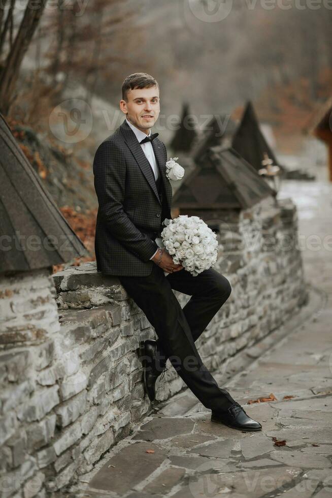 stilvoll Bräutigam. Porträt. vorbereiten zum das Hochzeit Zeremonie. Porträt im Natur. Bräutigam im ein schwarz Jacke. das Bräutigam mit ein Strauß im seine Hände foto