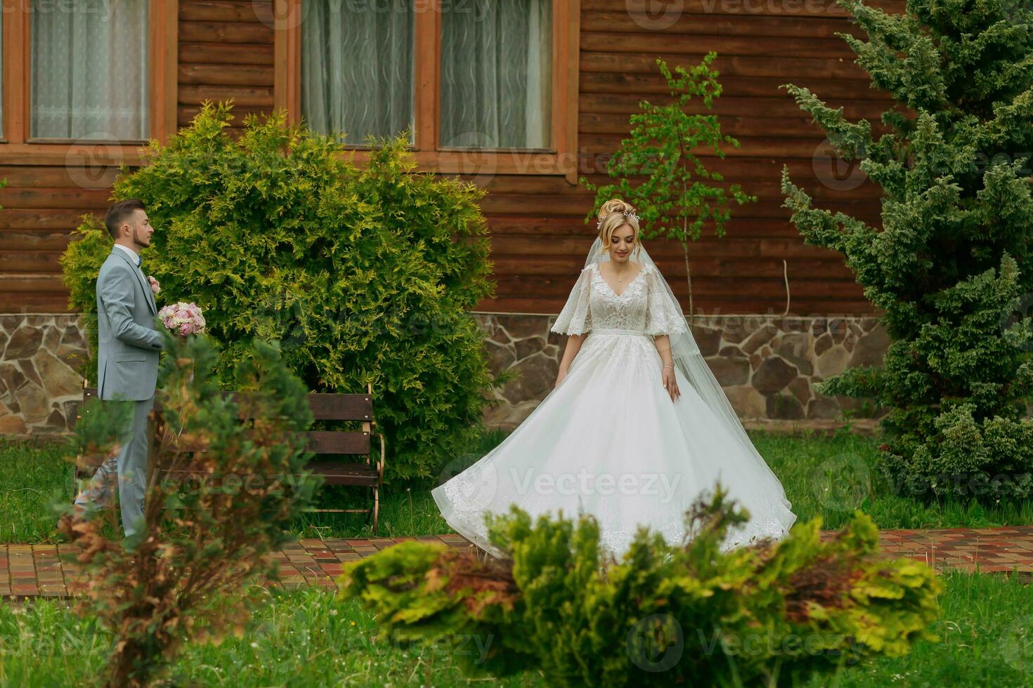 Hochzeit im Natur. Foto von das Braut und Bräutigam auf ein gehen gegen das Hintergrund von Bäume, das Braut geht zu Treffen das Bräutigam, gegen das Hintergrund von Bäume und ein hölzern Hütte. stilvoll Bräutigam.