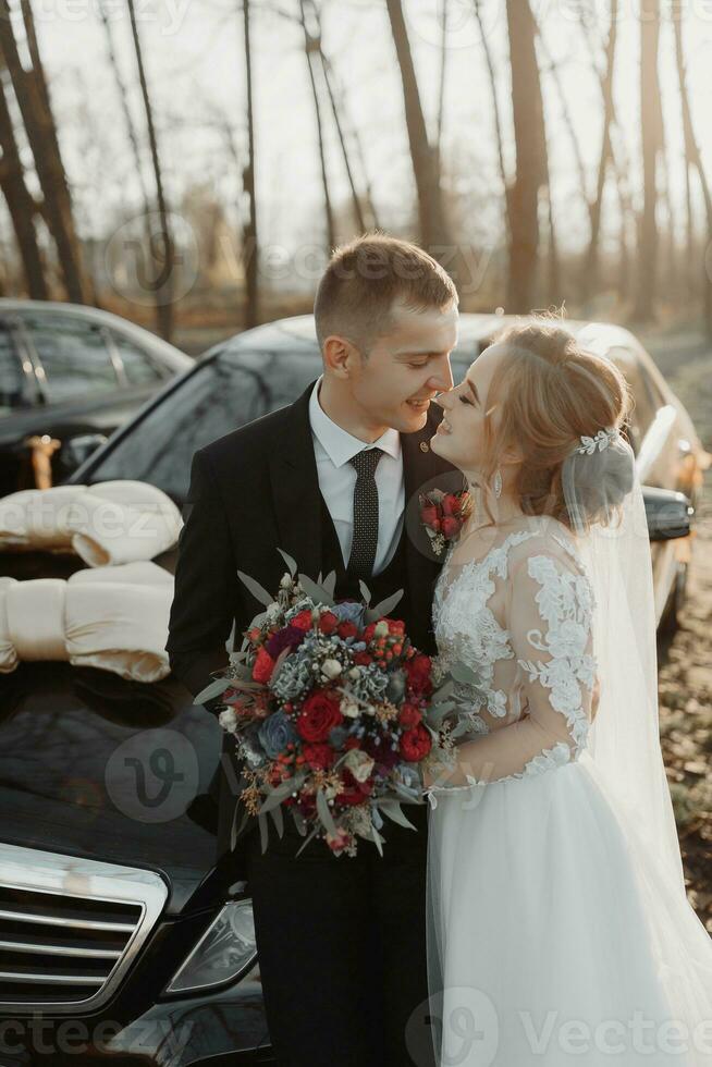 Herrlich Braut mit modisch bilden und Frisur im Luxus Hochzeit Kleid mit gut aussehend Bräutigam in der Nähe von schwarz Hochzeit Auto foto