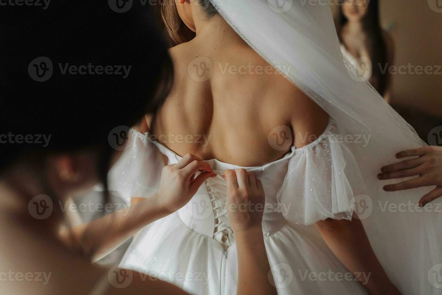 das Braut freunde befestigen das Weiß voluminös Kleid von das Braut. Rückseite Sicht. öffnen Schultern. schön Hände. lange Schleier. Morgen von das Braut. foto