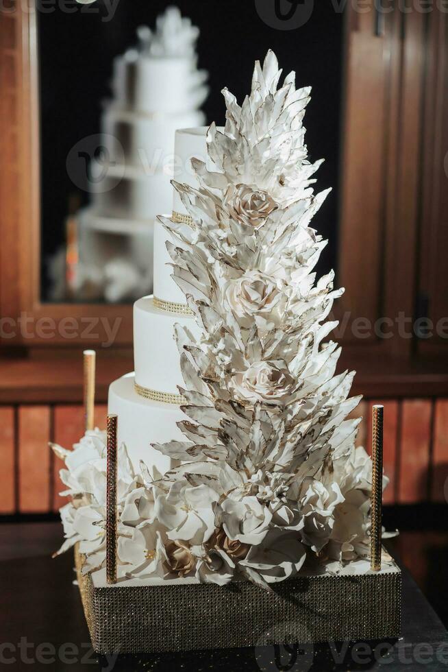 Weiß königlich Hochzeit Kuchen dekoriert mit Blumen und dekorativ Gefieder gemacht von Schokolade dekoriert mit Gold, auf ein Gold Stand. königlich Hochzeit, Süßigkeiten foto