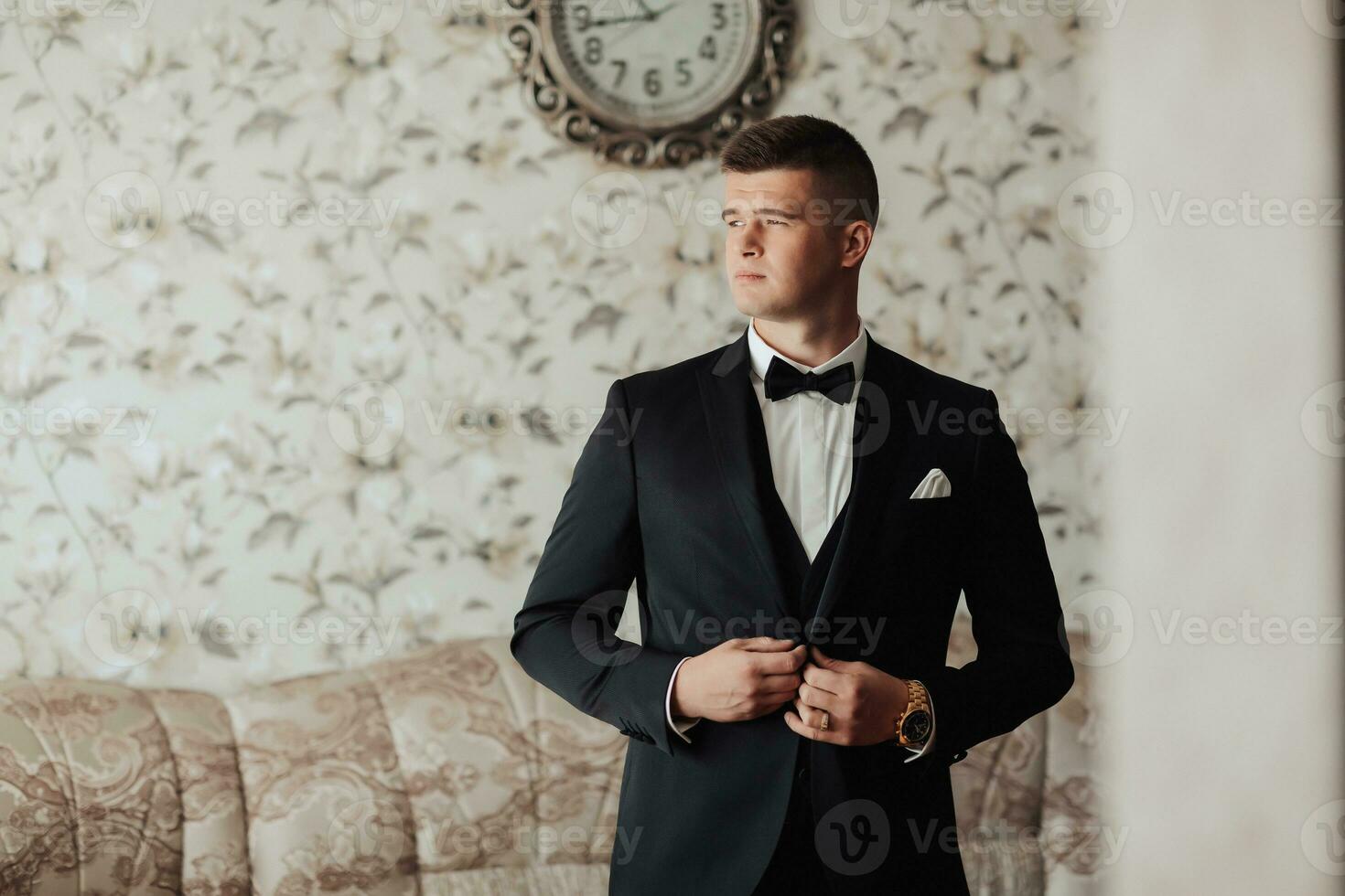 Porträt. ein Mann im ein Weiß Shirt, ein schwarz Bogen Krawatte und ein schwarz passen posiert im ein Zimmer. ein stilvoll betrachten. Herren Stil. Mode. Geschäft foto