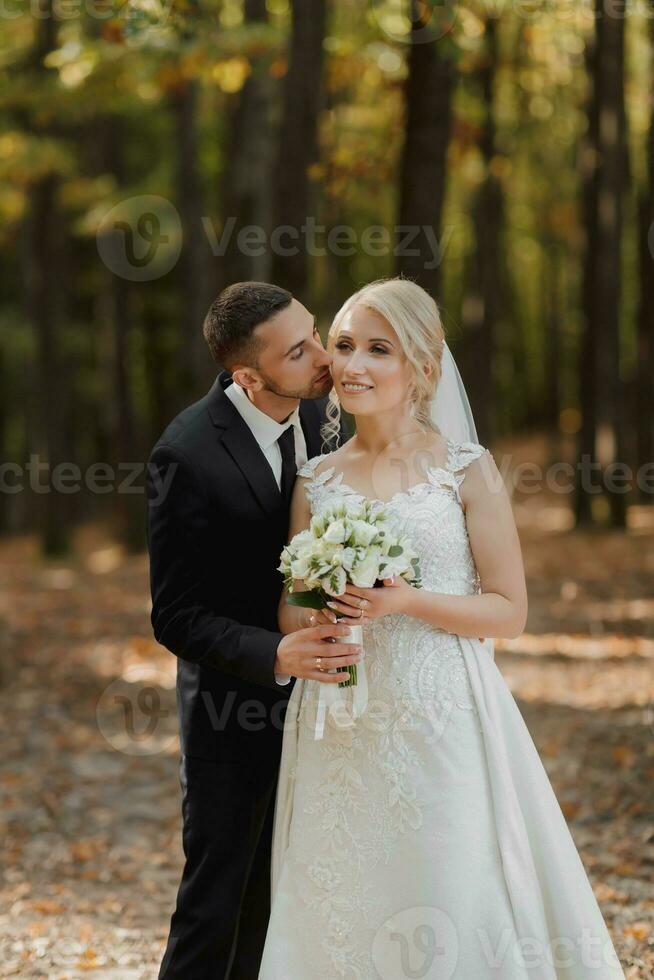 das Braut und Bräutigam gegen das Hintergrund von ein Märchen Nebel im das Wald, er Küsse ihr auf das Wange. das Strahlen von das Sonne brechen durch das Rauch, ein Märchen Hochzeit. foto