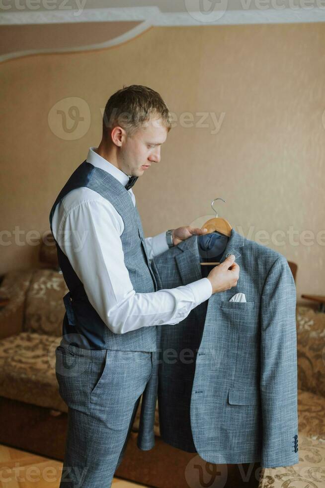 stilvoll Bräutigam Porträt bekommen bereit im das Morgen zum Hochzeit Zeremonie. Morgen von das Bräutigam. Bräutigam Morgen Vorbereitung. das Bräutigam setzt ein schwarz Jacke im Bewegung. Herren Mode, Herren Zubehör foto